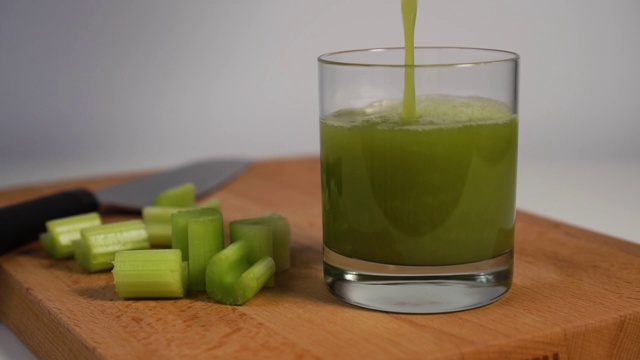 用刀将鲜榨的芹菜汁倒入放在木板上的玻璃杯中，然后切成多汁的薄片视频下载