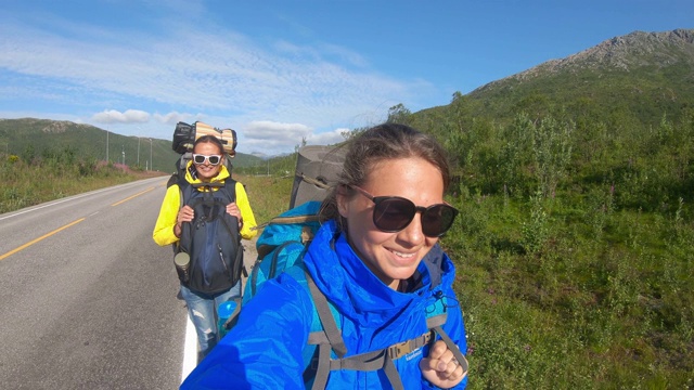两个年轻的女性旅行博主在挪威的一条路上自拍。视频下载