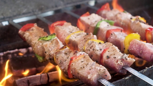 用烤肉串刺穿的美味猪肉串。肉中加入红、黄、青椒，撒上香料。用火舌在木炭烤架上的明火上烤。食物中有蒸汽。视频素材