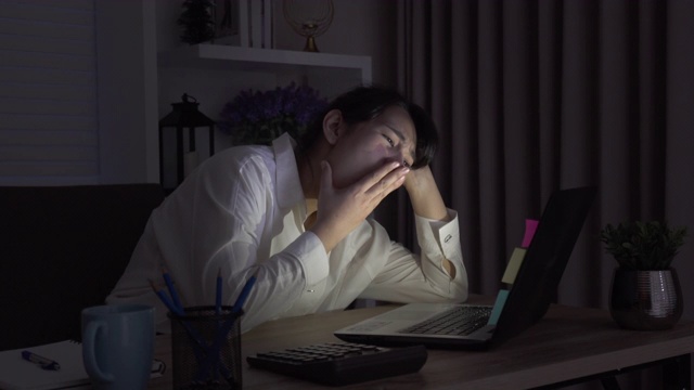 年轻的亚洲女性睡在她的房间或办公室的桌子上，在黑暗中。学习到深夜。熬夜。超负荷工作。会议的最后期限。视频下载