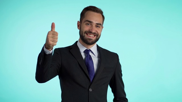 成功的快乐的人看着镜头，在蓝色的背景上竖起大拇指。职业男性经理穿着公司西装外套。商人孤立在工作室。视频素材