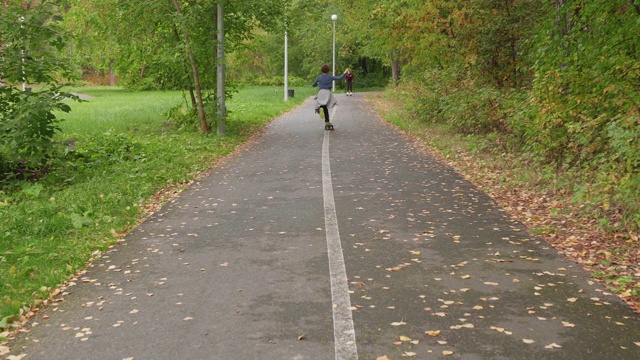 少年滑板在城市公园的后视图。后视图男孩少年骑滑板在小路上在绿色夏季公园。青年运动的生活方式。视频素材