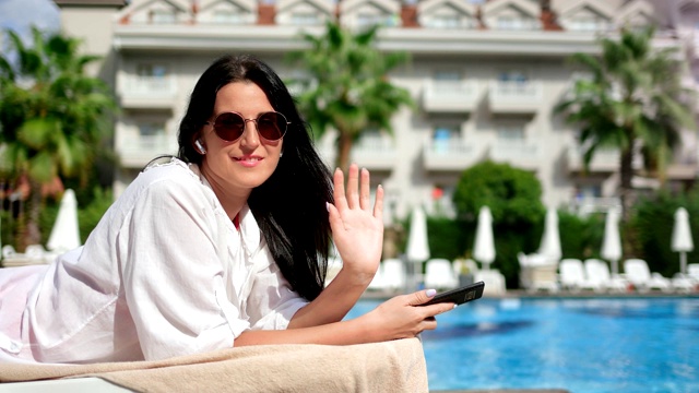 快乐的旅行女人的肖像摆在甲板上挥手在蓝色的水棕榈酒店的背景视频素材
