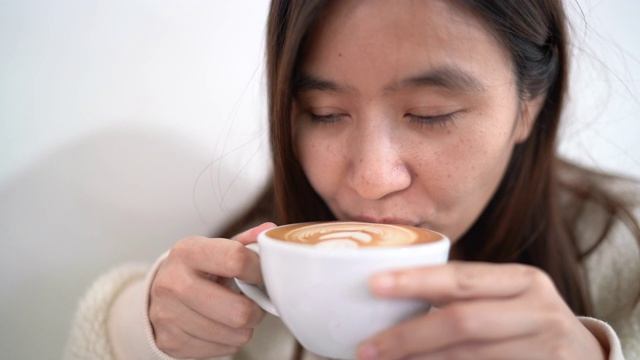 亚洲年轻女子在咖啡馆拿铁和喝热拿铁咖啡在冬天视频素材