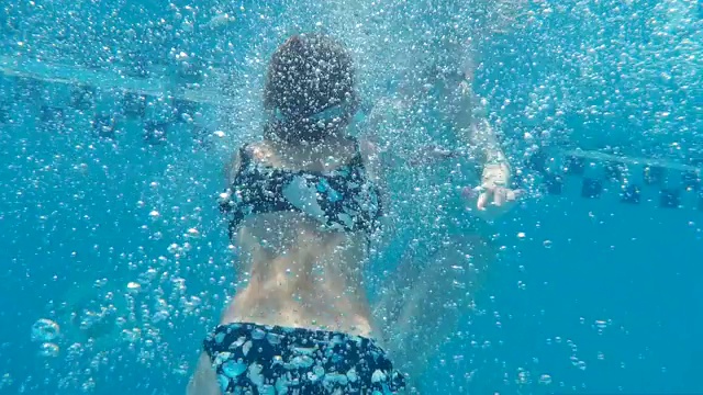 可爱的少女穿着泳衣在蓝色的游泳池里游泳视频下载