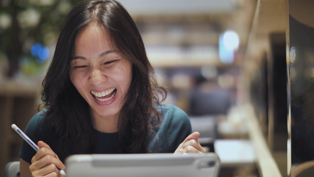 兴奋快乐的亚洲女人看着数字平板电脑兴奋地表达获胜的姿态视频素材