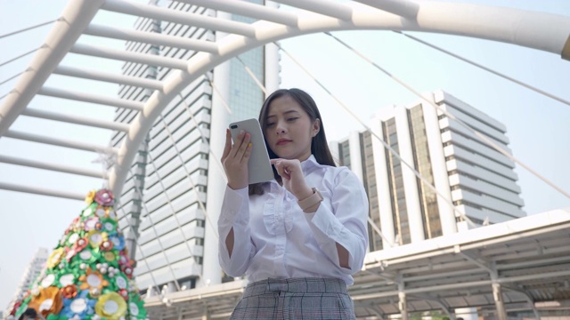 兴奋的商业亚洲女人跳庆祝好消息检查智能手机在现代的市中心在泰国曼谷晚上。技术沟通，成功靠手机视频素材