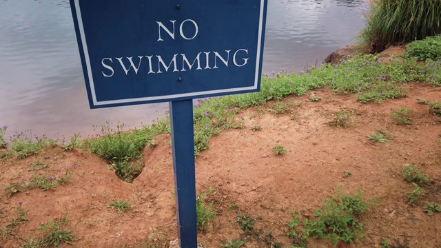 一个蓝色的禁止游泳的标志张贴在一个安静的男子池塘在郊区的住宅开发。视频下载