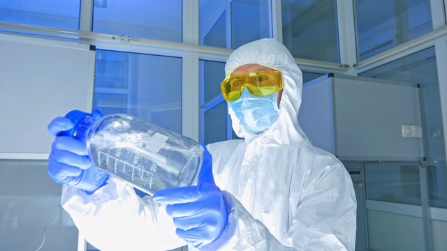 化学实验室-身着防护服检查反应瓶的科学家视频素材