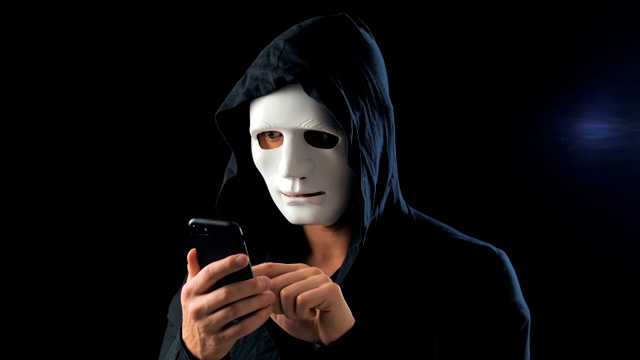 一名蒙面匿名诈骗犯使用智能手机进行勒索，要求赎金。蒙面罪犯利用手机短信威胁受害者。视频下载