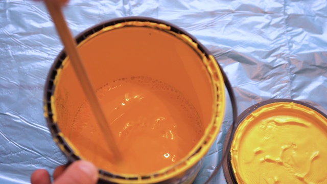 油漆工用一根棍子在罐子里搅拌黄色的墙漆。视频素材
