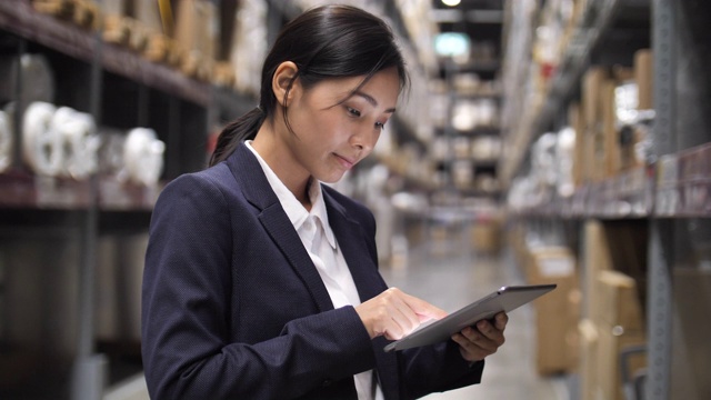 智能仓库管理:商务亚洲女性手握数字平板电脑在仓库视频素材