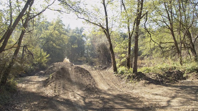MS摩托车越野赛车手在树林里阳光明媚的土路上视频素材