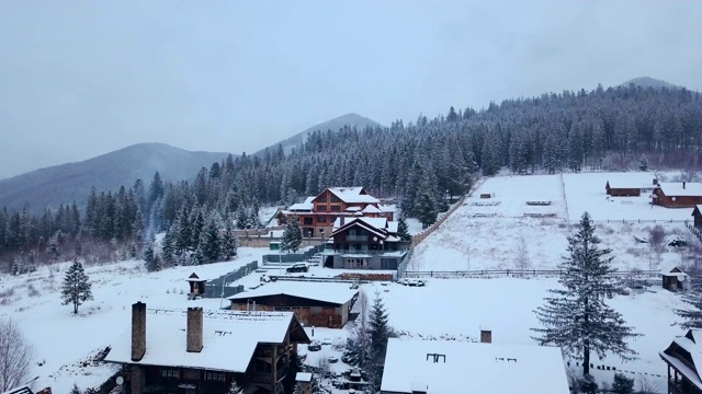 冬季山区有人居住地区的空中航拍。山村的建筑物和房屋在雪坡上覆盖着雪。乡村，冷杉和松树林。滑雪胜地的小屋视频下载