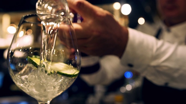近距离的调酒师测量杜松子酒在一个杯子，把它倒进鸡尾酒杯视频下载