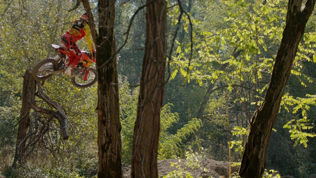 越野摩托车骑手在阳光明媚的树林里跳跃，飞过赛道视频素材
