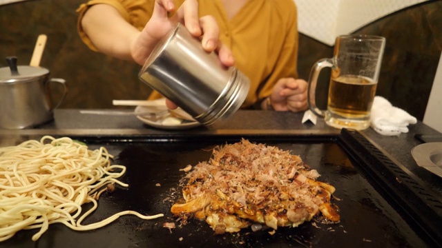 在日式餐厅里，一名年轻女子将“青苔”海带放在御好烧上视频素材
