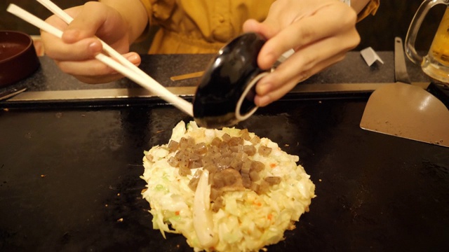 在日本餐馆里，一名年轻女子正在把“宫烧”放在御好烧上视频素材