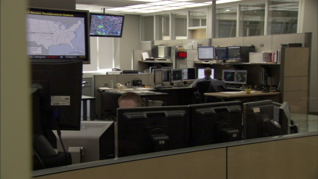 气象学家在他们的办公室里工作，旁边是电脑屏幕上的天气雷达图像和天气图。视频下载