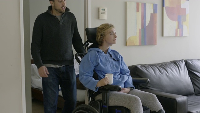 一对年轻夫妇在公寓客厅里，女人坐在轮椅上。视频下载