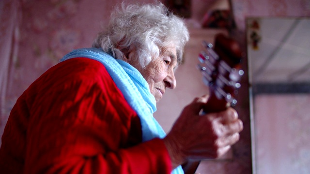 一个老人在弹吉他。音乐和娱乐。一个有皱纹的祖母的肖像，享受音乐和玩得开心。视频素材
