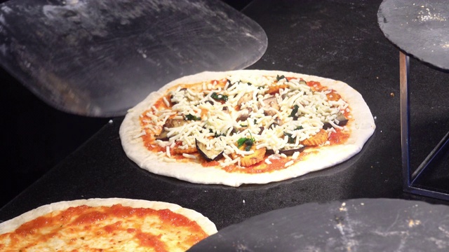 4K厨师烹饪披萨。厨师准备的披萨面团与肉，奶酪和蔬菜，放置在传统砖披萨烤箱烘烤在厨房为客户服务的意大利餐厅。视频素材