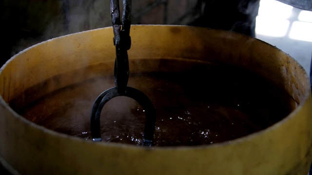 在一个铁匠铺里，一个马蹄铁被放在一个装有蜂蜡的大圆锅里，用来冷却熔化的铁。它会产生大量的蒸汽。视频下载