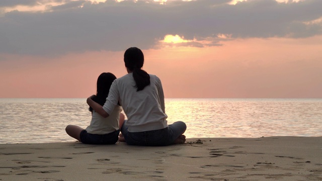 剪影快乐的母亲和女儿坐在海边的沙滩上玩日落海浪。积极的父母和人在暑假与孩子户外活动。幸福的家庭假期。家庭、生活方式、人、人寿保险、假期视频素材