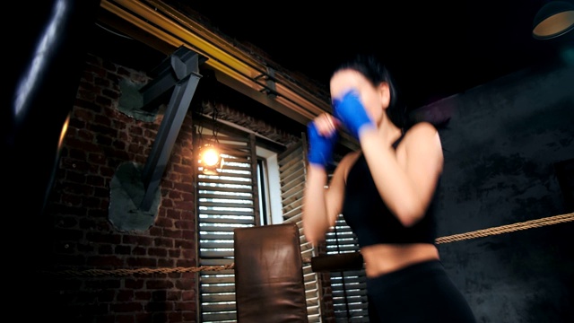 迷人的健美拳击手女人与完美苗条的身体打击拳击袋在黑暗的健身房室内视频下载