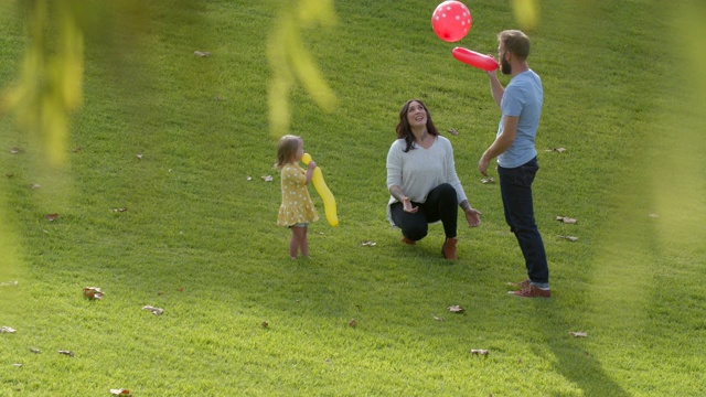 一个年轻的家庭和唐氏综合症的女儿在公园里玩气球视频素材