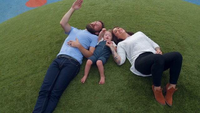 一个年轻的家庭和患有唐氏综合症的女儿一起躺在草地上视频素材