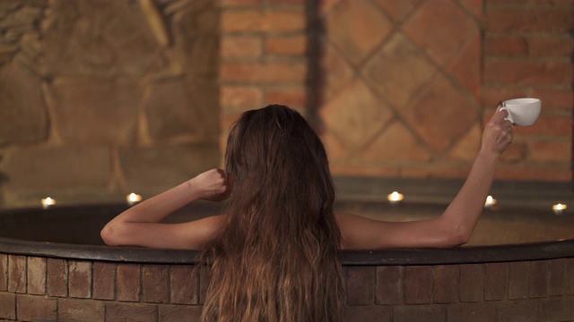 一个年轻的女人在温泉喝香茶的特写镜头，同时洗热水澡。水疗和健康。孤立的,模糊的背景视频下载