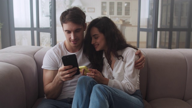 幸福的夫妇坐在沙发上一起玩手机。视频素材