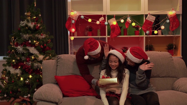 在圣诞节，父母闭上眼睛送一个礼物盒给他们的女儿一个惊喜。幸福的家庭视频素材