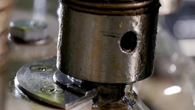 一个圆形金属喷嘴的特写向上和向下移动，并填充塑料瓶在一个石油生产工厂的传送带。视频下载