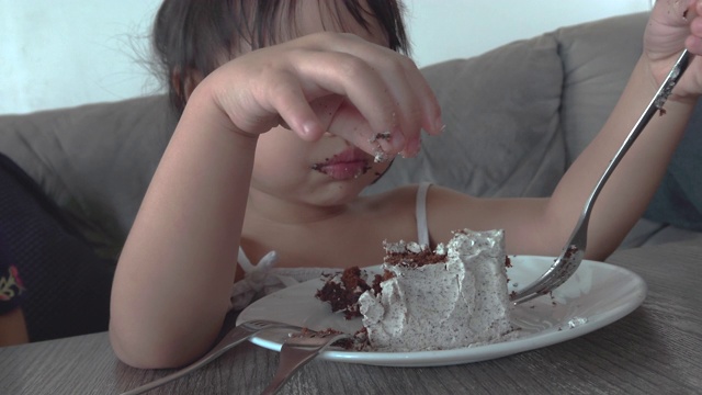 亚洲小女孩快乐地吃着蛋糕。幸福的家庭的概念。手持拍摄，真实现场视频素材