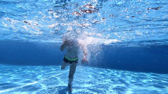 男孩在游泳池清澈的水下游泳。视频下载
