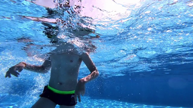 一个男孩在碧蓝清澈的水中游泳的水下视频。视频下载