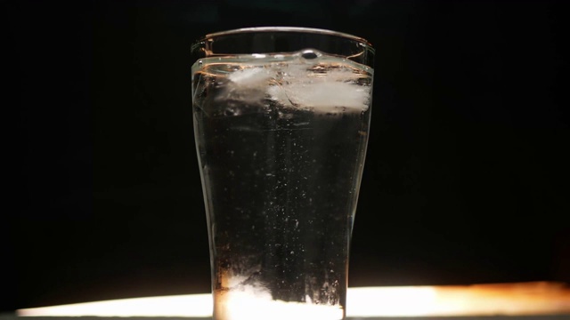 特写手扔冰块到一个玻璃与水，孤立在黑色背景。视频素材