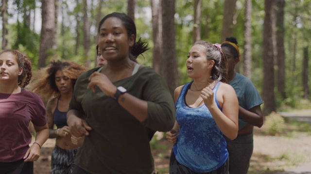 慢。铜。一位健康的女士在和一群女运动员一起在森林小路上跑步时，正在查看她的智能手表视频下载