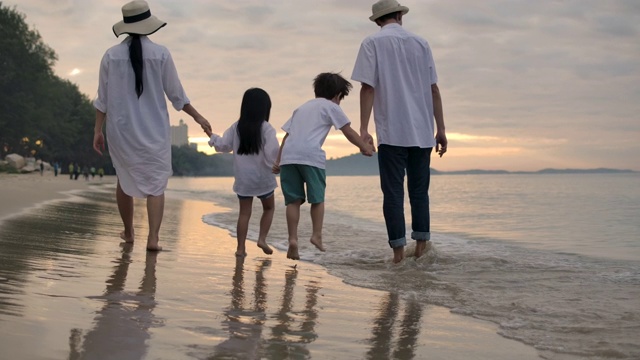 快乐的一家人在夏日日落时沿着海滩散步。缓慢的运动。视频素材