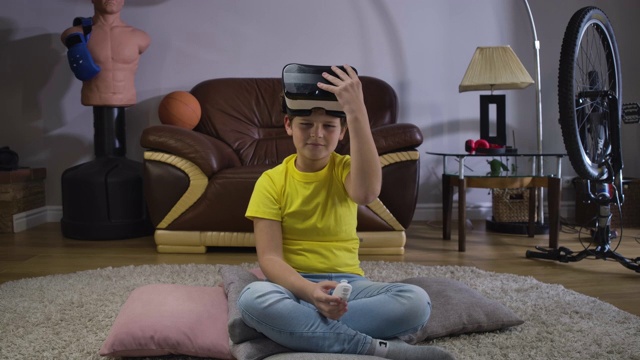 男性白人青少年的肖像采取VR头盔和使用远程控制打开游戏。孩子在家里试用设备。虚拟耳机，网络游戏，3d现实。电影4k ProRes总部。视频素材