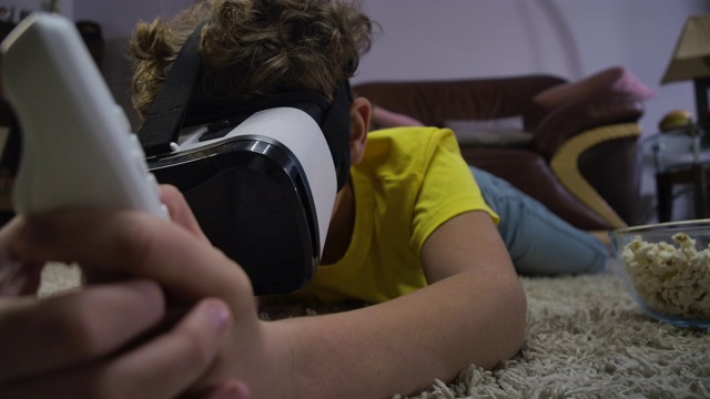 特写的十几岁的白人男孩躺在地板上，戴着VR头盔，拿着遥控器。孩子玩虚拟现实游戏。Z一代、游戏。电影4k ProRes总部。视频素材