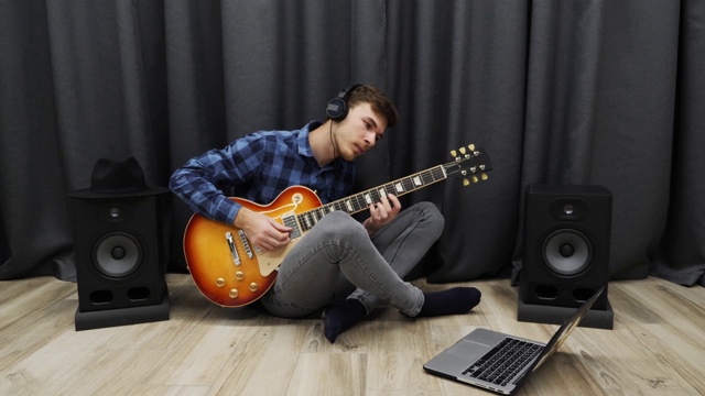 学习弹吉他的人。年轻男子戴着耳机用笔记本弹电吉他。一个少年坐在客厅的地板上学习吉他和弦视频下载