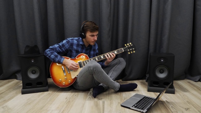 人类正在学习弹吉他。戴着耳机的男人在练习电吉他。一个年轻人坐在客厅的地板上弹吉他视频下载