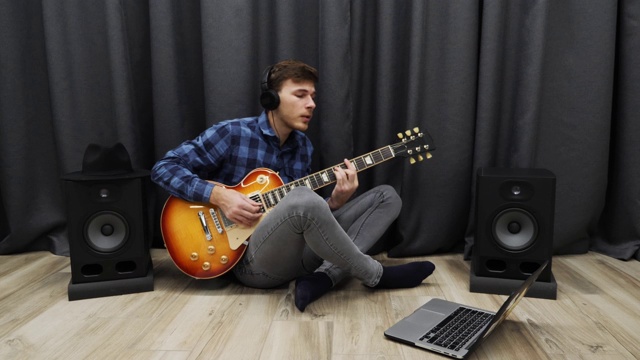 戴着耳机的男人一边弹吉他一边唱歌。专业的音乐家用电吉他练习歌曲，坐在客厅里唱歌。吉他音乐课程视频下载