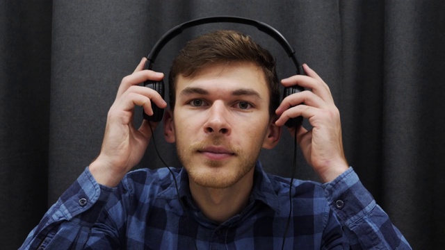 男人戴着耳机听音乐的肖像。年轻的微笑男子戴着耳机，听着灰色背景的歌曲视频下载