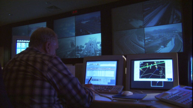 交通中心的一名工作人员坐在一排电脑监视器前，上面显示着来自交通摄像头的视频。视频下载
