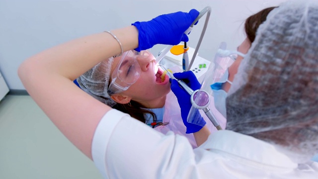 牙科保健师为牙科的年轻女性提供超声波清洁牙齿的服务。视频素材