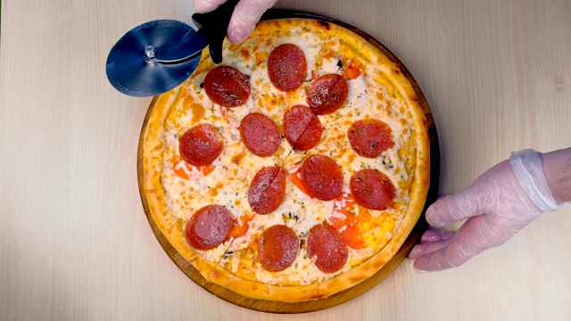 厨师将意大利腊肠披萨切成片。双手在橡胶手套近景俯视图。视频素材